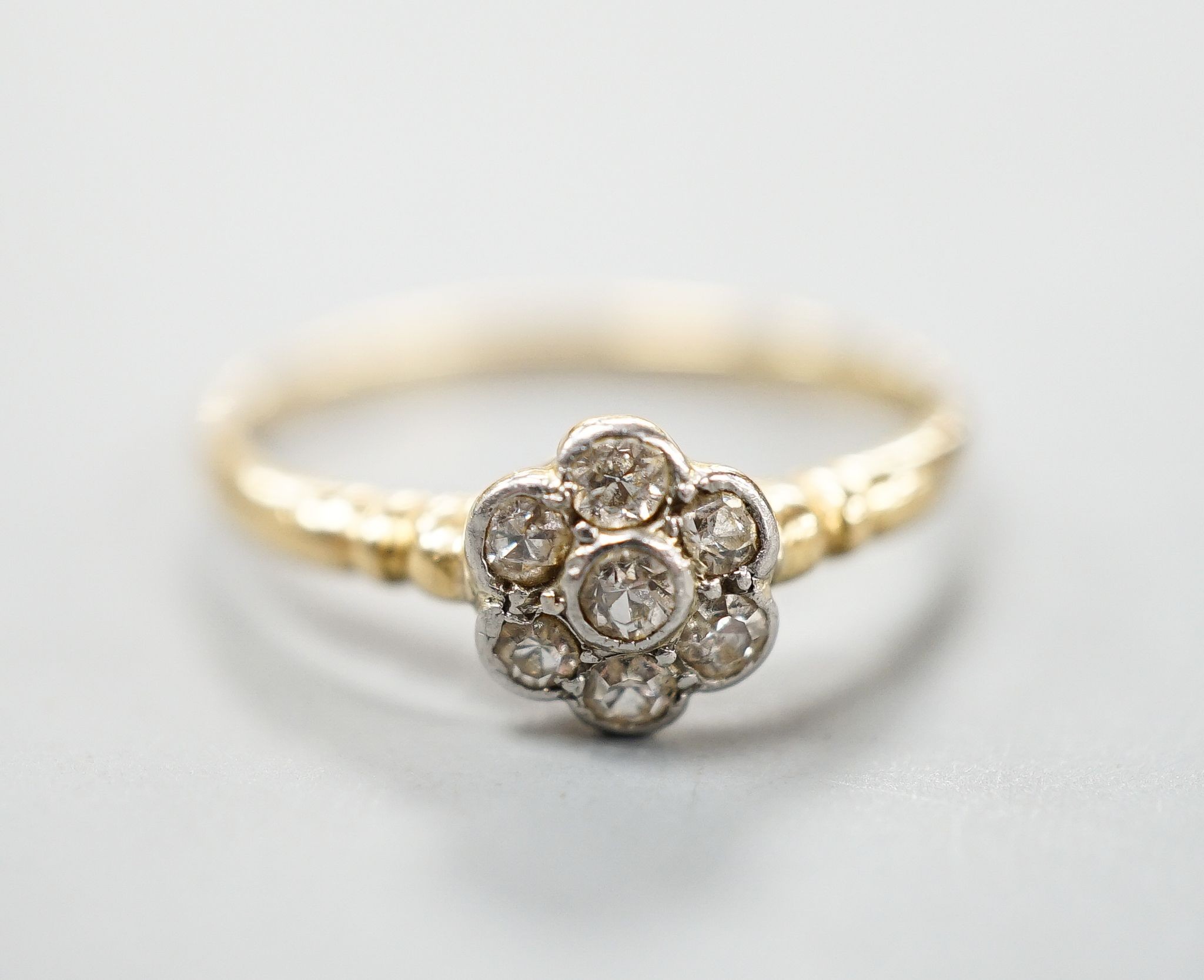 An 18ct and seven stone diamond cluster set flower head ring, size O, gross weight 2.3 grams.